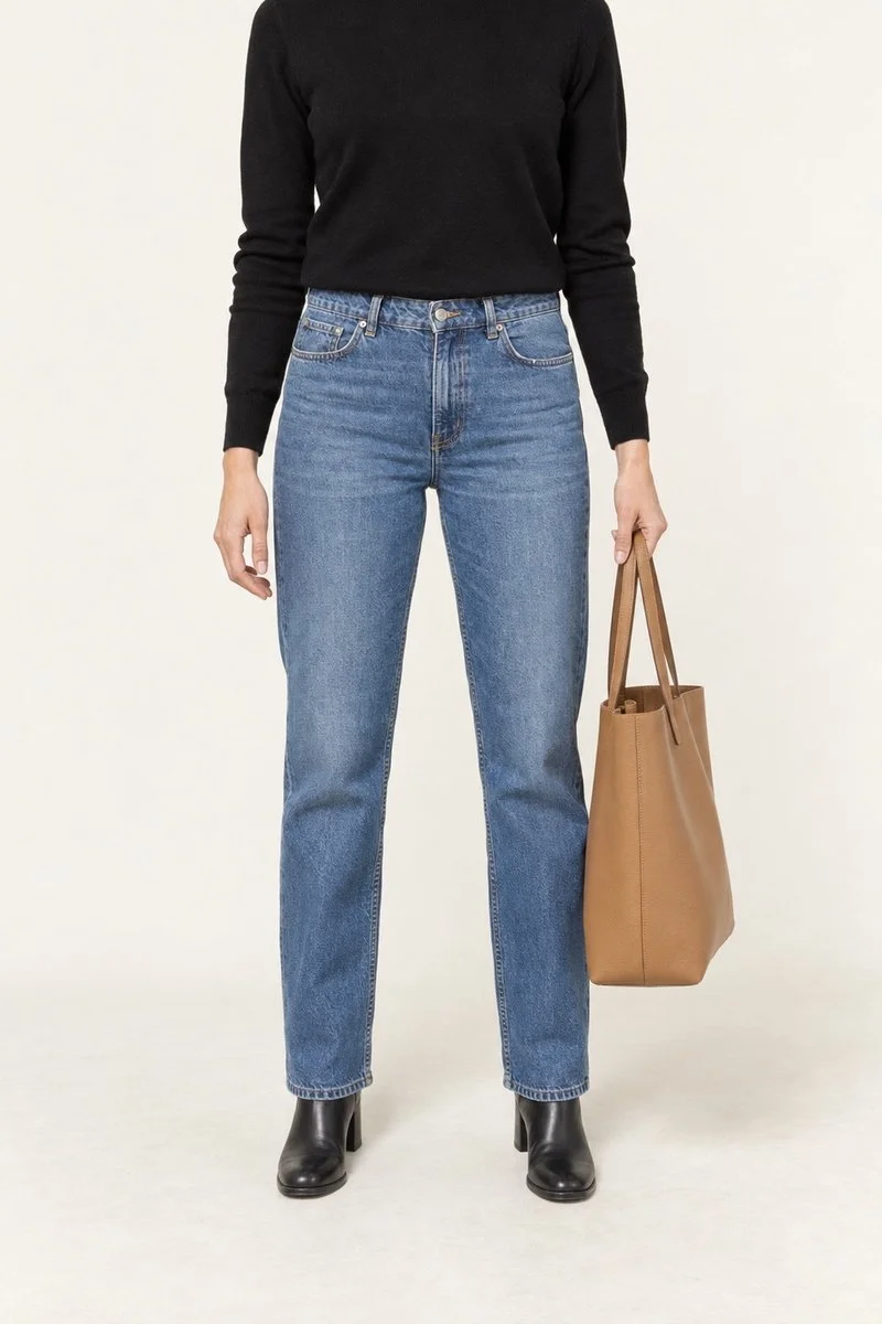 An illustrative outfit photograph: black knit, blue jeans, ankle boots and a tan tote.